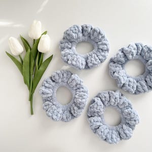 May include: Four light blue fuzzy scrunchies, also known as hair ties, on a white surface.