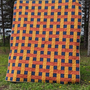 May include: A large quilt with a checkered pattern in shades of yellow, orange, and blue. The quilt is made of squares with a swirling pattern inside each square.
