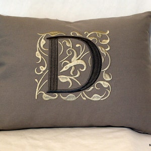May include: A gray pillow with a black embroidered letter D surrounded by a gold floral design.