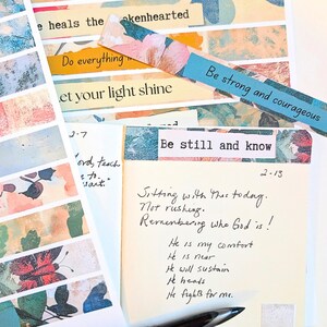 May include: A collection of inspirational notes and decorative paper strips. The strips feature floral and abstract designs with phrases like "Be strong and courageous" and "Be still and know." A handwritten note includes the text "Sitting with this today. Not rushing."