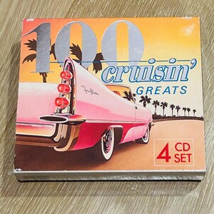 Może przedstawiać: Zestaw płyt CD zatytułowany "100 Cruisin' Greats" z ilustracją r&oacute;żowego zabytkowego samochodu. Okładka albumu ma retro design z palmami i tłem zachodu słońca. Zestaw zawiera 4 płyty CD.