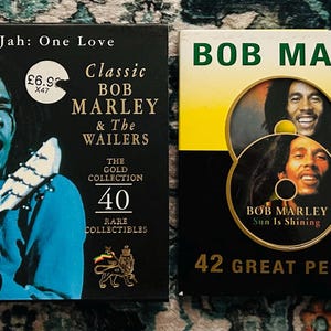 Może przedstawiać: Dwa płyty CD z muzyką Boba Marleya. Jedna obudowa CD jest czarna ze zdjęciem Boba Marleya grającego na gitarze i tekstem "Classic Bob Marley & The Wailers". Druga obudowa CD jest czarna i ż&oacute;łta ze zdjęciem Boba Marleya i tekstem "Sun Is Shining".