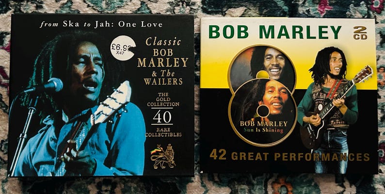Może przedstawiać: Dwa płyty CD z muzyką Boba Marleya. Jedna obudowa CD jest czarna ze zdjęciem Boba Marleya grającego na gitarze i tekstem "Classic Bob Marley & The Wailers". Druga obudowa CD jest czarna i ż&oacute;łta ze zdjęciem Boba Marleya i tekstem "Sun Is Shining".