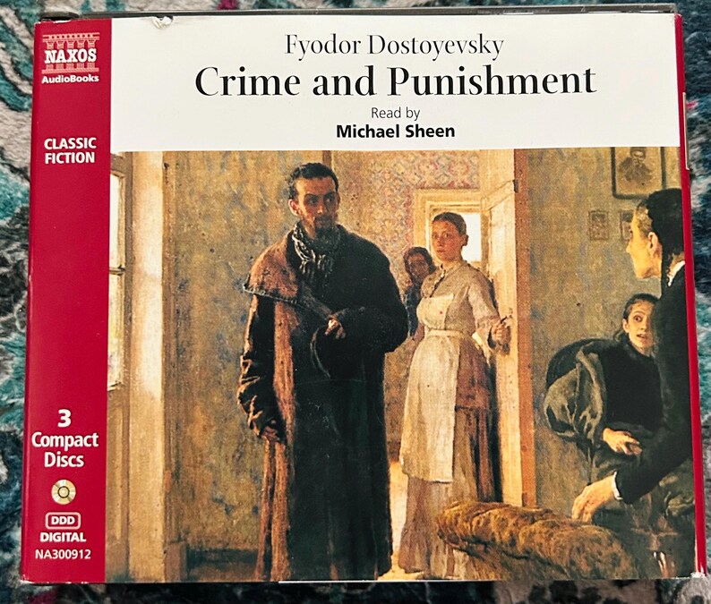 May include: A boxed audiobook of "Crime and Punishment" by Fyodor Dostoevsky, read by Michael Sheen. The cover shows a painting of a room with several people. The box is red and white with the Naxos Audiobooks logo and "Classic Fiction" text.