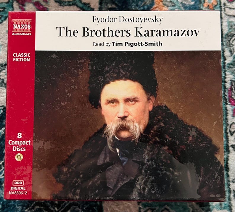 May include: A boxed set of "The Brothers Karamazov" audiobook by Fyodor Dostoyevsky, read by Tim Pigott-Smith. The cover features a portrait of a man with a large mustache. The box is red and white with the Naxos Audiobooks logo and the text "Classic Fiction".