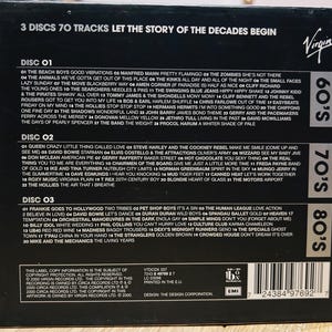 Może przedstawiać: Czarny zestaw płyt CD z napisem "3 Discs 70 Tracks Let the Story of the Decades Begin". Zawiera 3 płyty z utworami z lat 60., 70. i 80. Widoczne jest logo Virgin.