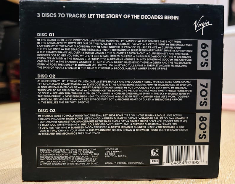 Może przedstawiać: Czarny zestaw płyt CD z napisem "3 Discs 70 Tracks Let the Story of the Decades Begin". Zawiera 3 płyty z utworami z lat 60., 70. i 80. Widoczne jest logo Virgin.