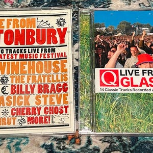 Może przedstawiać: Dwa krążki CD z muzyką "Live From Glastonbury". Jedna obudowa CD ma czerwono-biały design z nazwiskami artyst&oacute;w, takich jak Amy Winehouse. Druga obudowa CD ma zdjęcie tłumu na festiwalu muzycznym z tekstem "Live From Glastonbury".