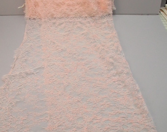 May include: A piece of pink lace fabric with a delicate, intricate pattern. The lace is sheer and has a soft, flowing texture.