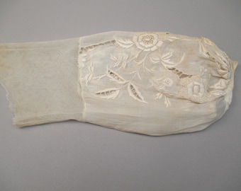 May include: An antique off-white sleeve, likely from a garment, featuring intricate floral embroidery. The sleeve is made of a sheer, delicate fabric with a detailed floral design and cut-out patterns. The sleeve is slightly stained.