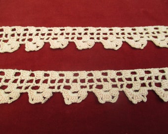 May include: Two pieces of delicate, off-white crochet trim with a scalloped edge. The trim has a square pattern with a small flower design in the center of each square.
