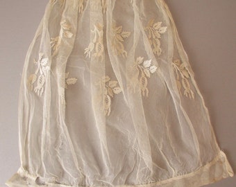 May include: A delicate white lace bonnet with a floral design. The bonnet is made of a fine mesh fabric and has a scalloped edge.
