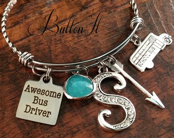 May include: Silver charm bracelet with a turquoise blue gem, a school bus charm, an arrow charm, and a charm with the letter "S" encrusted with rhinestones. The bracelet also has a square charm with the text "Awesome Bus Driver".