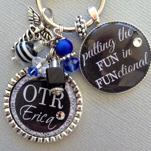 May include: A silver keychain with a black and white striped bead, blue beads, and two round black charms. One charm says "putting the FUN in FUNCTIONAL" and the other says "OTR Erica".