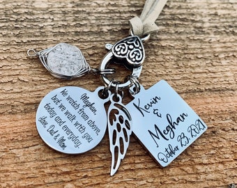 May include: A silver charm necklace with a heart-shaped clasp, a small angel wing charm, a round charm with the text "Meghan, We watch from above, but we walk with you today and everyday. Love, Dad & Mom", and a square charm with the text "Kevin & Meghan October 23, 2021".