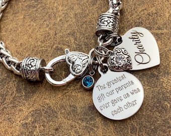 May include: Silver chain bracelet with a heart charm that says "Charity" and a round charm that says "The greatest gift our parents ever gave us was each other".