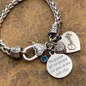 May include: Silver chain bracelet with a heart charm that says "Charity" and a round charm that says "The greatest gift our parents ever gave us was each other".