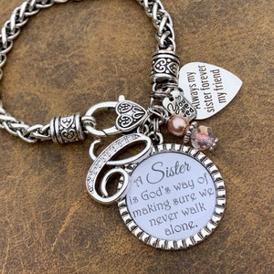 May include: A silver charm bracelet with a heart charm that reads "Always my sister forever my friend". The bracelet also has a charm with the text "A Sister is God's way of making sure we never walk alone."