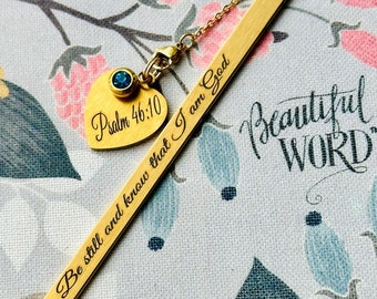 May include: Gold bookmark with a heart charm and a blue gemstone. The bookmark is engraved with the text "Psalm 46:10 Be still and know that I am God".