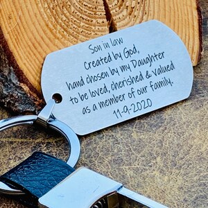 May include: A silver keychain with a black leather strap and a silver tag that reads "Son in law Created by God, hand chosen by my Daughter to be loved, cherished & valued as a member of our family. 11-9-2020"