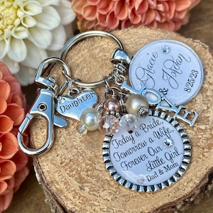 May include: A silver keychain with charms, including a heart charm with the word "Daughter", a round charm with the text "Today a Bride, Tomorrow a Wife, Forever Our Little Girl, Dad & Mom", and a round charm with the text "Gracie & Jordan 8/25/23".
