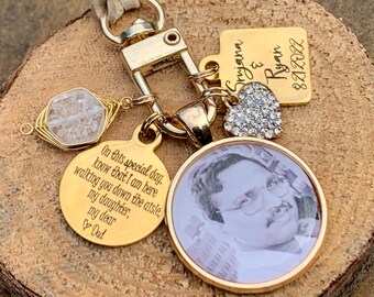 May include: Gold keychain with a photo charm, a small heart charm, a crystal charm, and a tag that says "On this special day, know that I am here walking you down the aisle, my daughter, my dear Dad." The tag also has the names "Srujana & Ryan" and the date "8.21.2022".