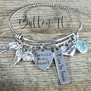 May include: Silver charm bracelet with multiple charms, including angel wings, a heart with the inscription "Forever in my heart", a tag with the inscription "I'll Love You Forever", a heart with the inscription "Special Mother", and a light blue crystal charm.