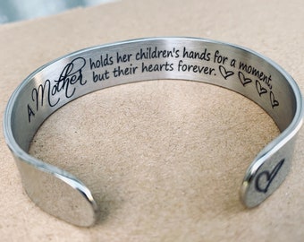May include: A silver bracelet with the inscription "A Mother holds her children's hands for a moment, but their hearts forever." and three heart symbols.