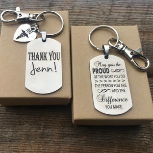 May include: Two silver keychains with engraved messages. One reads "THANK YOU Jenn!" and includes a heart-shaped charm with an RN symbol. The other keychain says "May you be PROUD...and the Difference YOU MAKE."