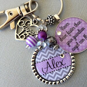 May include: Purple and silver keychain with a heart charm that says "Sweet 16", a round charm with a chevron pattern and the name "Alex", and a round charm with the text "Never drive faster than your guardian angel can fly".