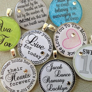 May include: A set of 10 round, silver-rimmed charms with various designs and text. The charms feature a green charm with the text "Ava for", a white charm with the text "Live for today", a blue charm with the text "We love you to the moon", a pink charm with a heart, a white charm with the text "A mother holds her child's heart forever", a white charm with the text "Sweet 16", and a white charm with the text "Jacob Lance Ramsey Locklyn".
