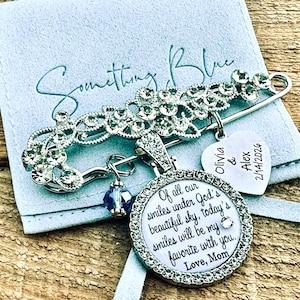 May include: A silver-tone safety pin brooch adorned with clear crystals, featuring a round pendant with the text "Of all our smiles under God's beautiful sky, today's smiles will be my favorite with you. Love, Mom" and a heart charm engraved "Olivia & Alex 2/14/2026".