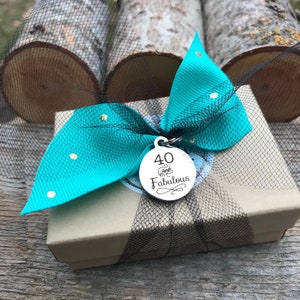 May include: A small gift box wrapped in brown paper with a turquoise bow and gold polka dots. A silver charm with the text "40 and Fabulous" is attached to the bow.