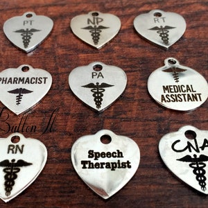 May include: Nine silver heart-shaped charms with different medical professions engraved on them, including RN, CNA, PA, PT, NP, RT, PHARMACIST, SPEECH THERAPIST, and MEDICAL ASSISTANT. Each charm features a medical symbol.