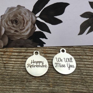 May include: Two silver round metal charms with engraved text. The charm on the left says "Happy Retirement". The charm on the right says "We Will Miss You".