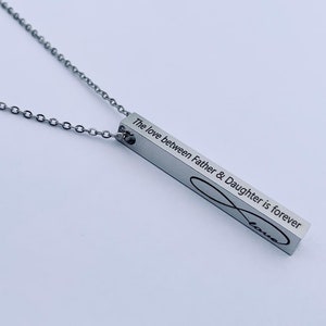 May include: Silver necklace with a bar pendant engraved with the text "The love between Father & Daughter is forever" and an infinity symbol with the word "love" inscribed inside.