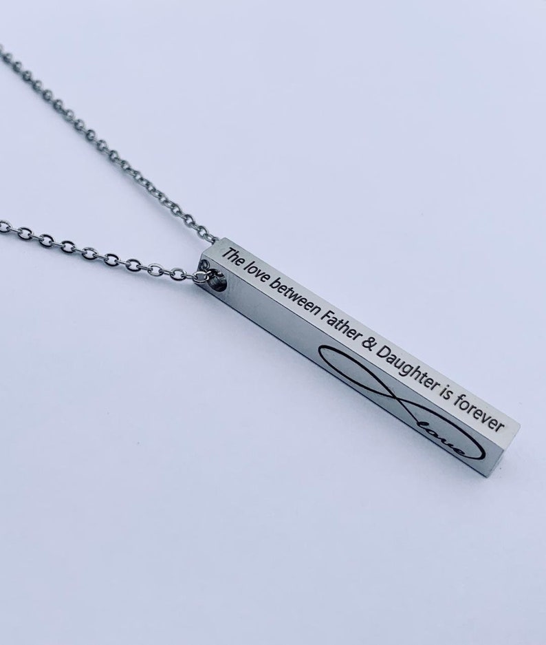 May include: Silver necklace with a bar pendant engraved with the text "The love between Father & Daughter is forever" and an infinity symbol with the word "love" inscribed inside.