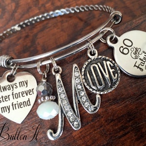 May include: Silver charm bracelet with a heart charm that says "Always my sister forever my friend", a charm with the letter "M" with rhinestones, a charm that says "LOVE", and a charm that says "60 and Fabulous".