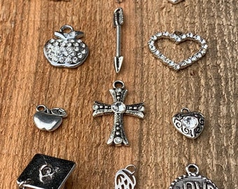 May include: Assortment of silver charm pendants, including a tree, cross, heart, apple, arrow, graduation cap, angel wing, and a circle with the word "LOVE".