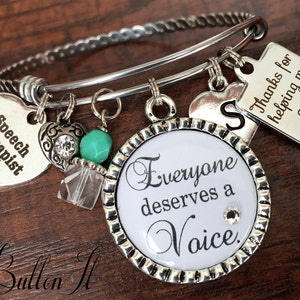 May include: Silver charm bracelet with a round charm that says "Everyone deserves a Voice." The bracelet also has a heart charm that says "Speech Therapist", a heart charm with a letter "S", and a square charm that says "Thanks for helping me grow".