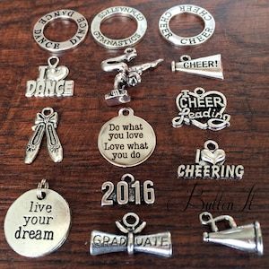 May include: A collection of silver charm pendants with various themes, including dance, cheerleading, gymnastics, and graduation. The charms feature words like "I Love Dance", "Cheer Leading", "Do What You Love", "Live Your Dream", and "Graduate".
