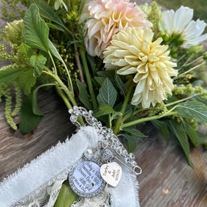 May include: A silver-toned brooch with clear crystals attached to a white lace ribbon, featuring a round charm inscribed with "Today a Bride, Tomorrow a Wife, Forever Our Little Girl, Mom & Dad" and a heart charm engraved with "Darby & Adel 10/06/26".