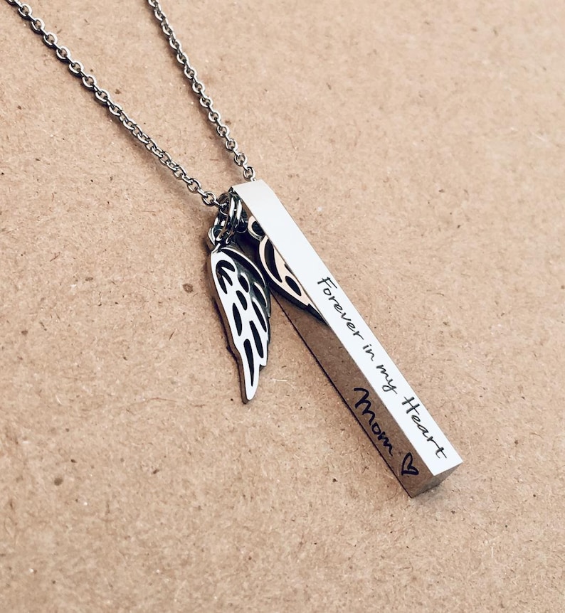 May include: Silver necklace with a vertical bar pendant engraved with "Forever in my Heart Mom" and a small angel wing charm.