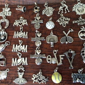 May include: A collection of silver charm pendants featuring various sports themes, including soccer, baseball, basketball, softball, volleyball, hockey, swimming, golf, lacrosse, and cheerleading. The charms are perfect for adding a personal touch to jewelry or crafts.