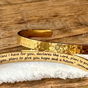 May include: Gold hammered metal bracelet with an engraved inspirational quote from Jeremiah 29:11, "For I know the plans I have for you, declares the Lord, plans to prosper you and not to harm you, plans to give you hope and a future."