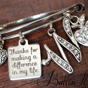 May include: Silver charm bracelet with a heart, an apple, a letter M, and a square charm with the text "Thanks for making a difference in my life".