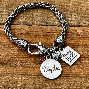 May include: A silver-toned wheat chain bracelet featuring a lobster clasp, a small red crystal charm, a heart-shaped charm, a round metal disc engraved with the name Mary Ann, and a square metal tag engraved with the text Vintage 1966.
