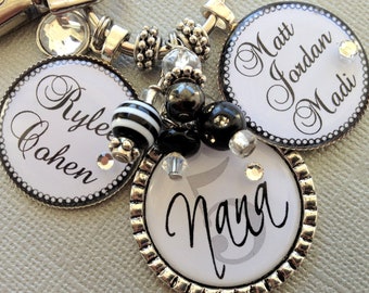 May include: A silver keychain with four round white and black charms. The charms have the names "Rylee Cahen", "Matt Jordan Madi", and "Nana" written in black cursive script. The keychain also has black and white beads and clear crystal beads.