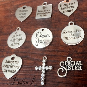 May include: Assortment of silver charm pendants with various sayings, including "Sisters of the Heart", "Friends are the sunshine of life", "Live Laugh Love", "I love you", "Remember the Moments", "Always my sister forever my friend", "Special Sister", and a cross charm with rhinestones.