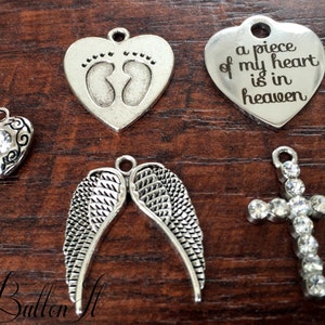 May include: Six silver charm pendants, including a heart with the text "a piece of my heart is in heaven", a heart with a crystal, a pair of angel wings, a cross with crystals, and a heart with two footprints.